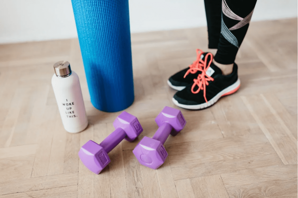 Woman standing at home with purple dumbells, a yoga matt, and other gym equipment