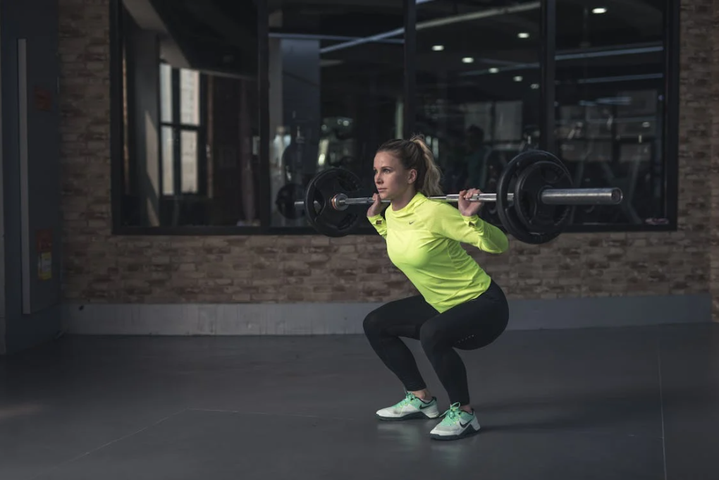 Women squatting a barbell in the gym to train and grow her glutes