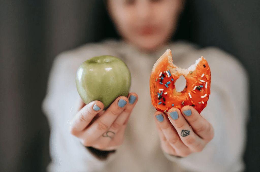 Women holding an apple and a donut while eating to create a calorie deficit